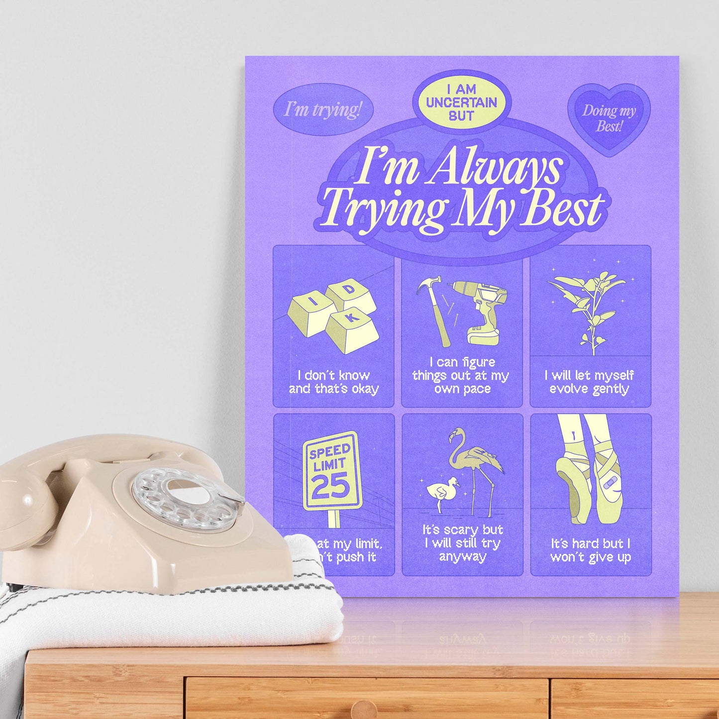 A self-care art print with the text "always trying my best" on a table next to a telephone