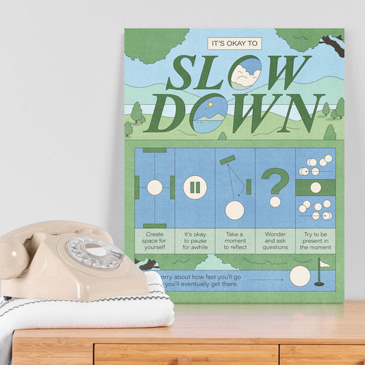 A self-care art print with the text "it's okay to slow down" on a table next to a telephone