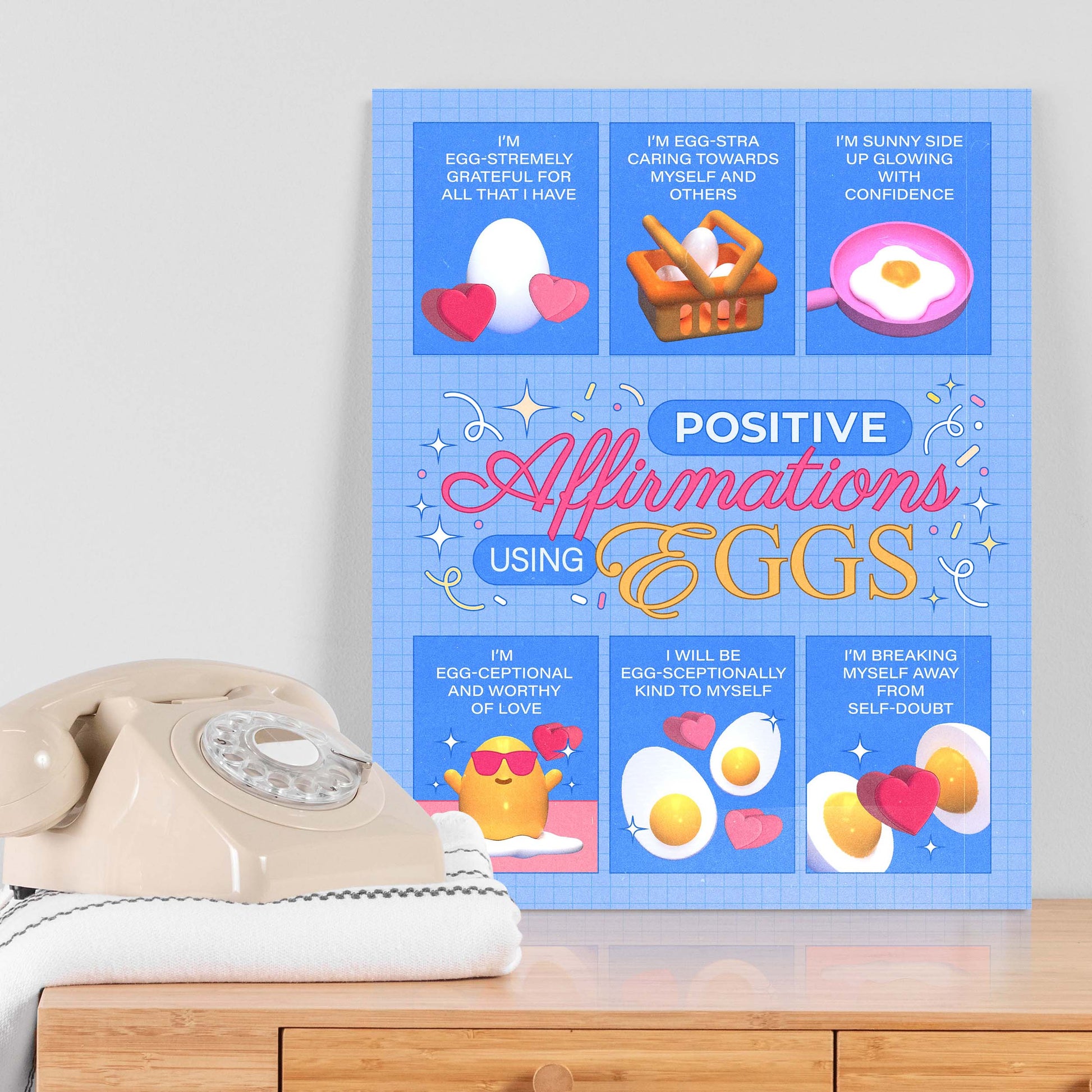 Blue self-care art print with the text "positive affirmations using eggs" on a table next to a telephone